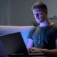 Young adult male with army dog tags working on laptop in dark room